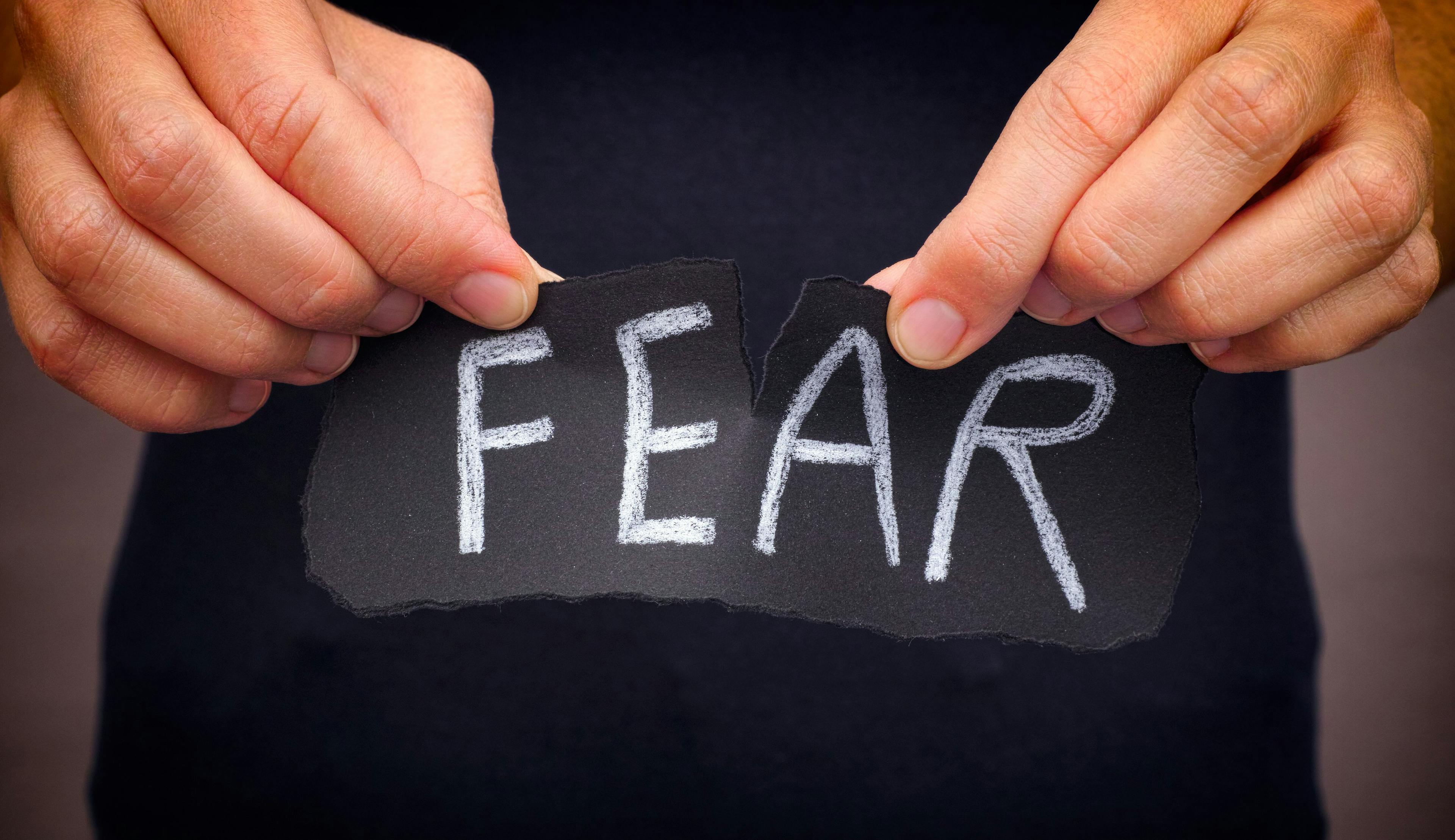 Image of a person ripping a piece of paper that says "fear."