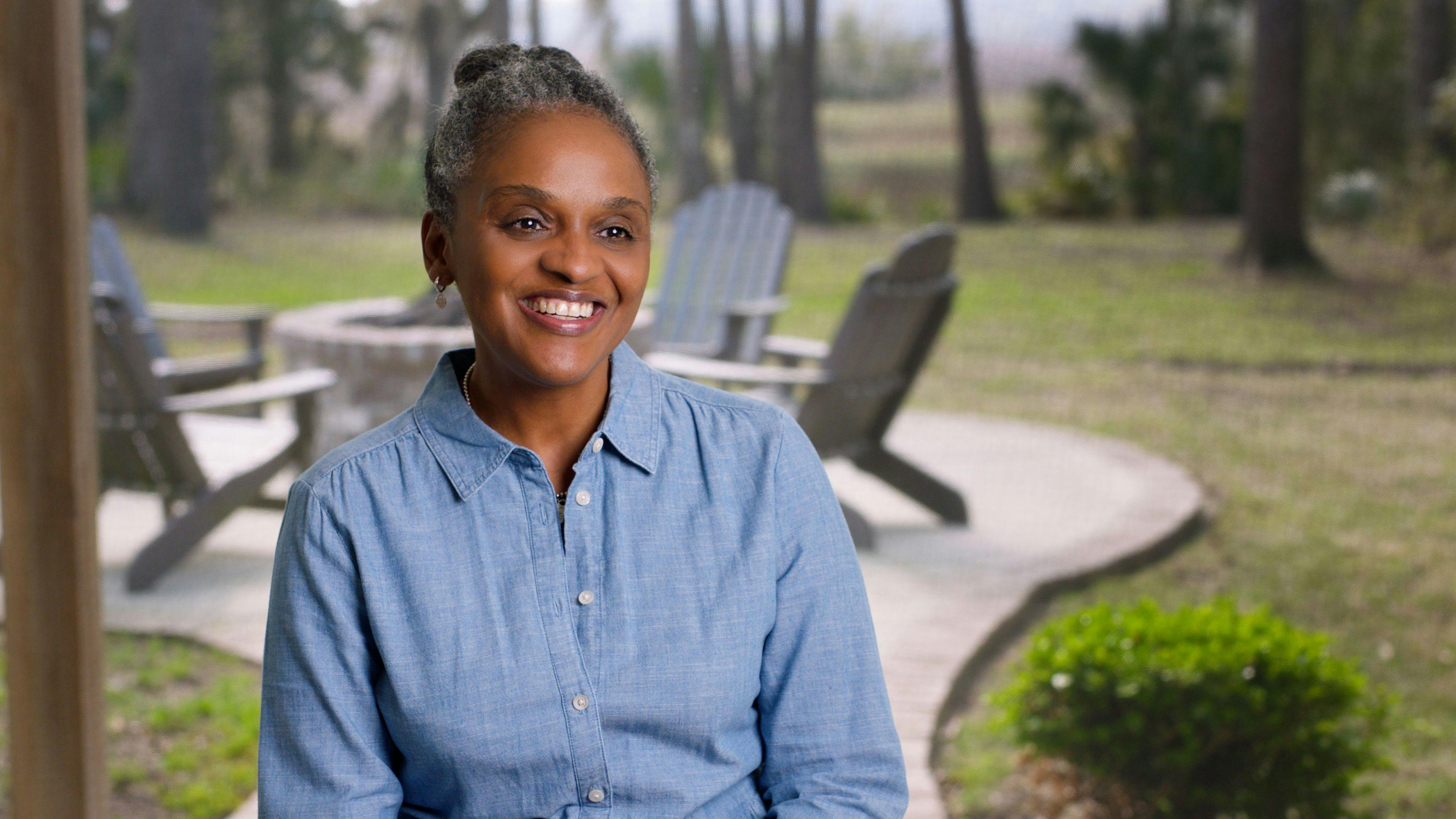 Tiffany Williams, a black woman with pulled back gray hair, smiling. She is sitting outside 