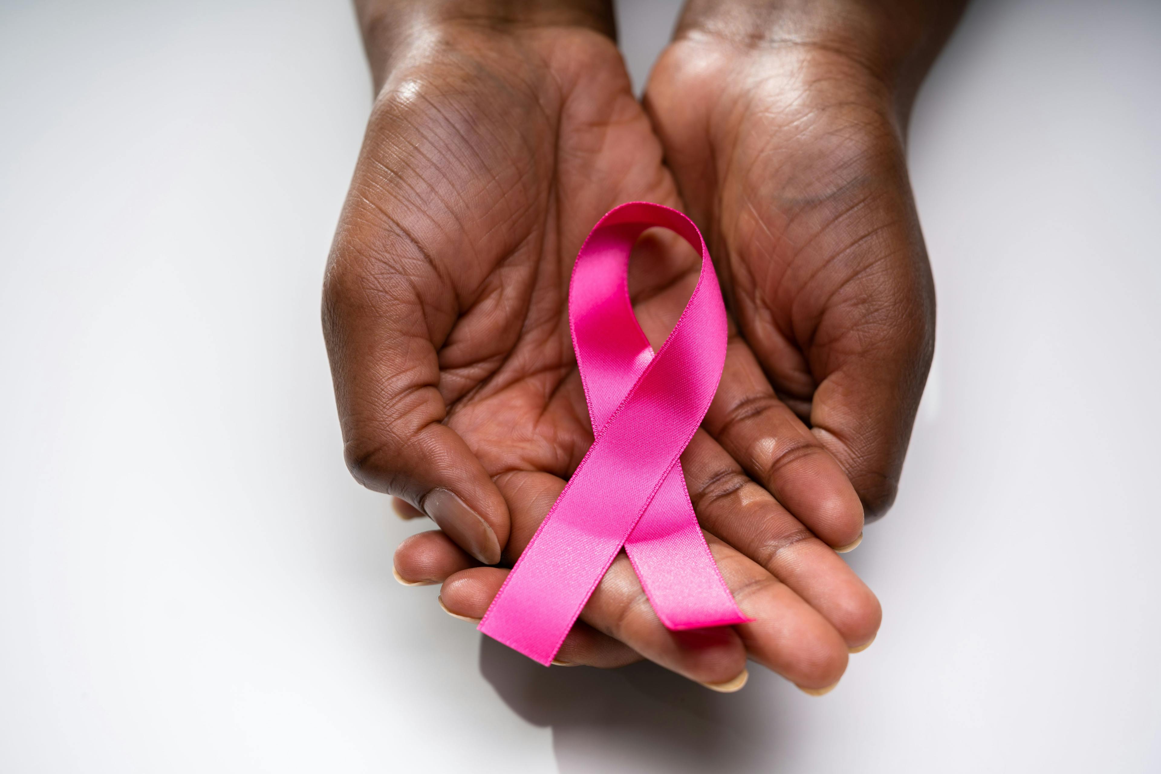 Black woman holding a pink ribbon in her hands, symbolizing breast cancer. 
