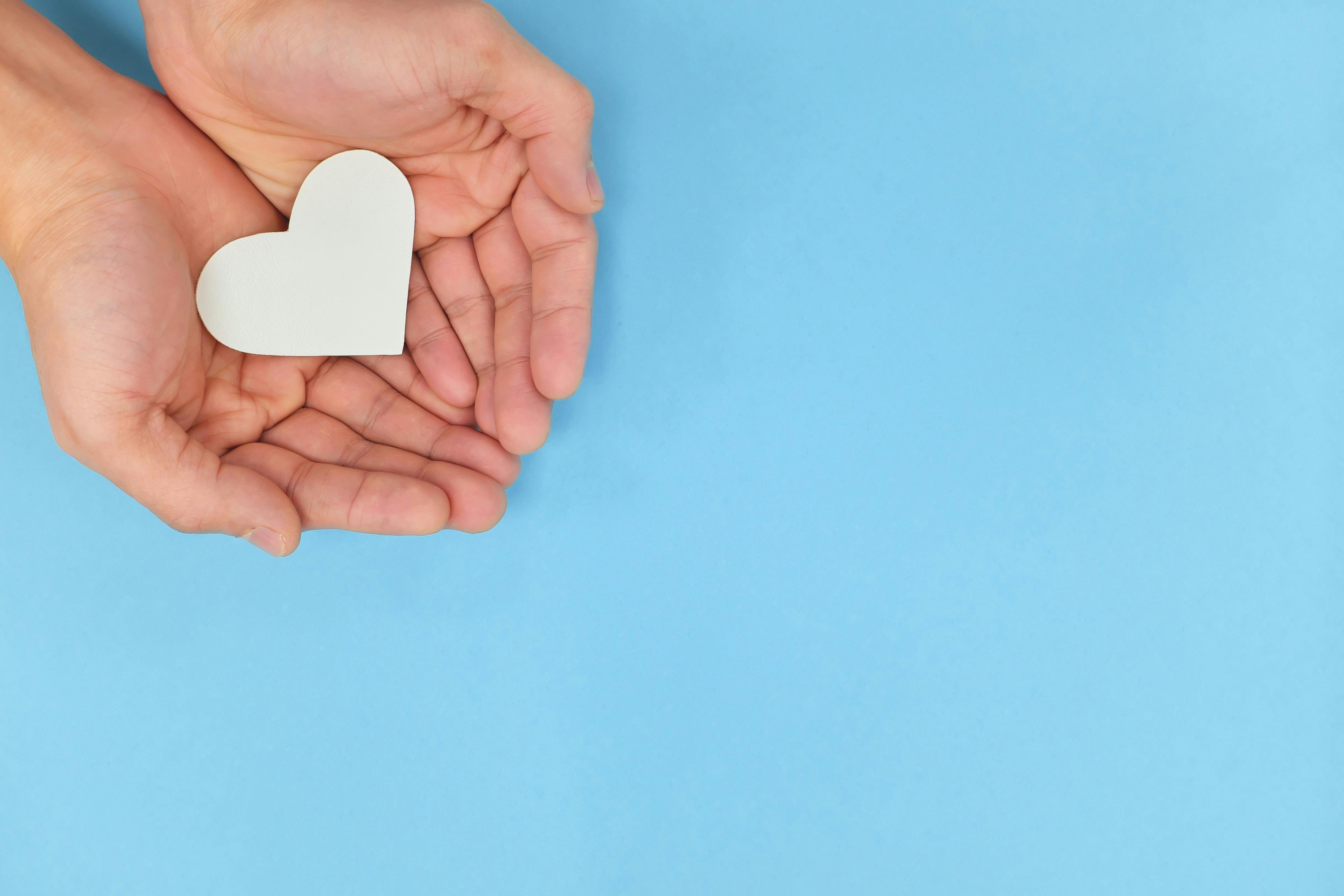 Image of a light blue background with a pair of hands cupping a paper heart.