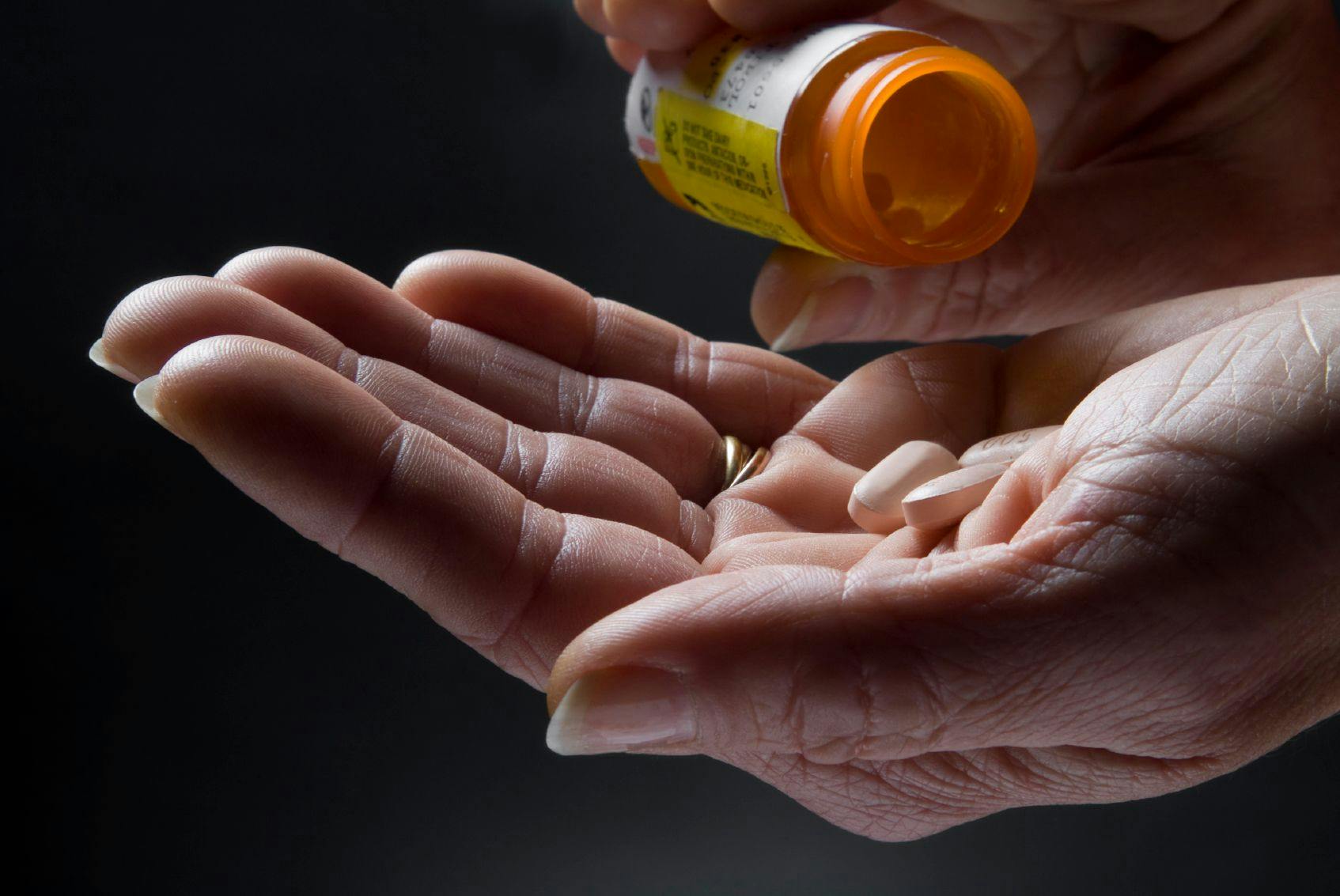 Image of a person pouring three pills into their hand from a pill bottle.