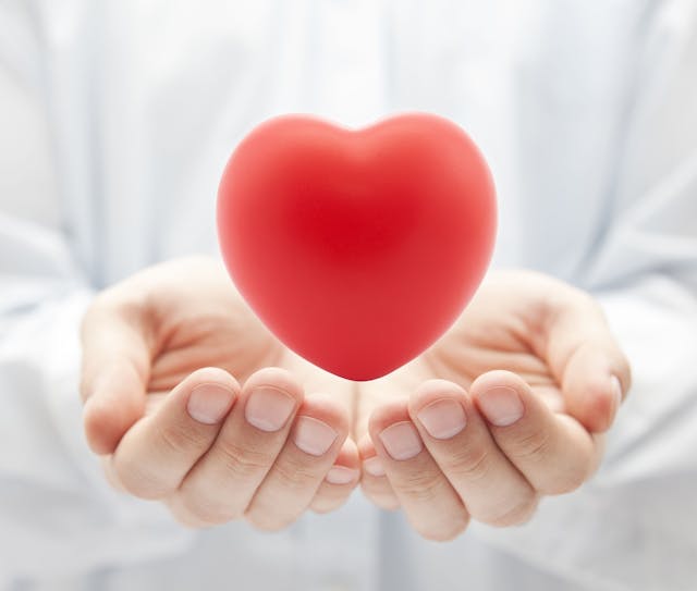 Image of a doctor cupping their hands around a red heart.