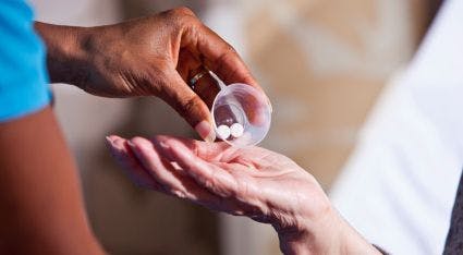nurse dropping two white pills into a patient's hand 
