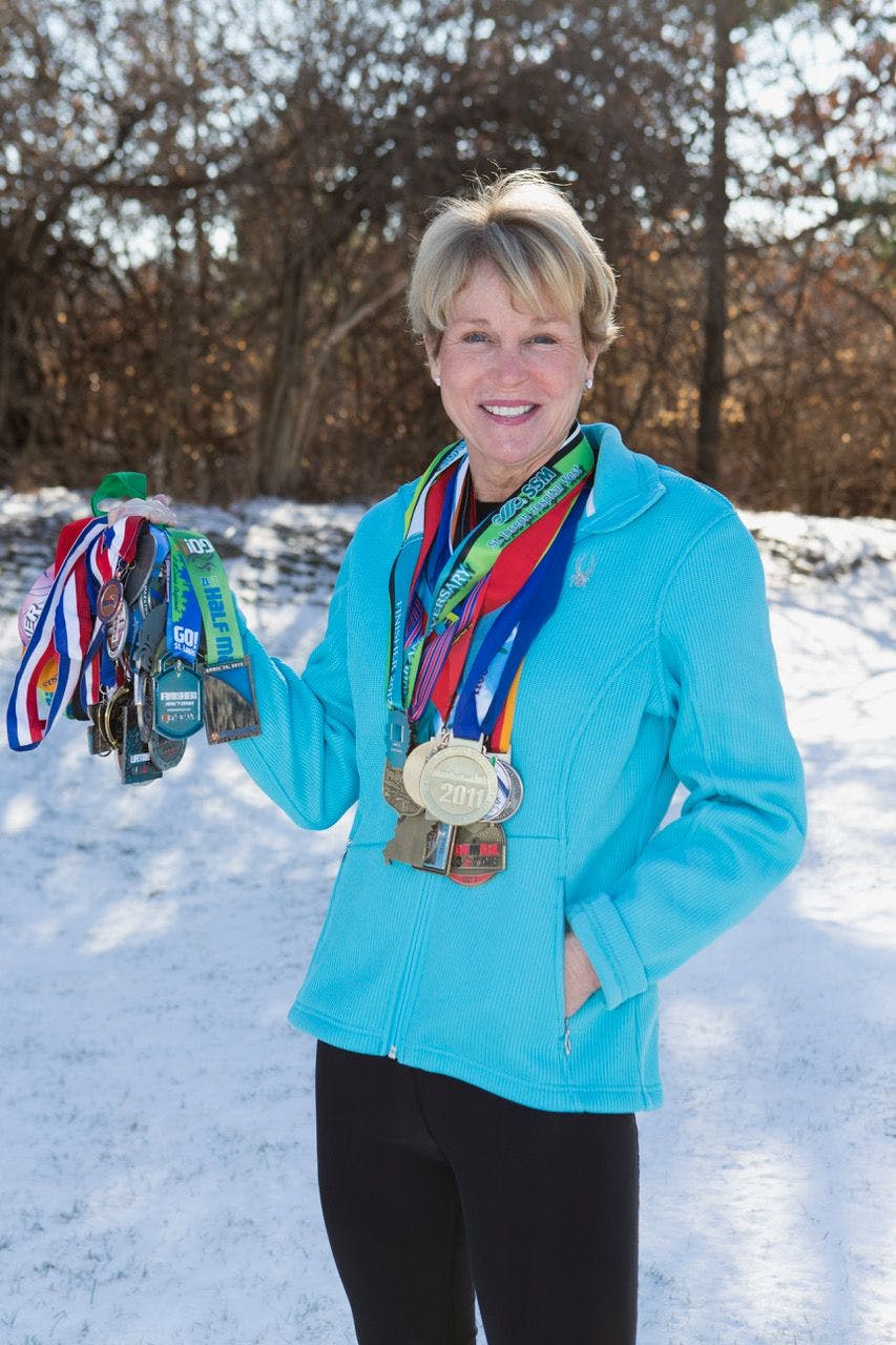 Teri Griege wearing a blue jacket showing off her many triathlon medals