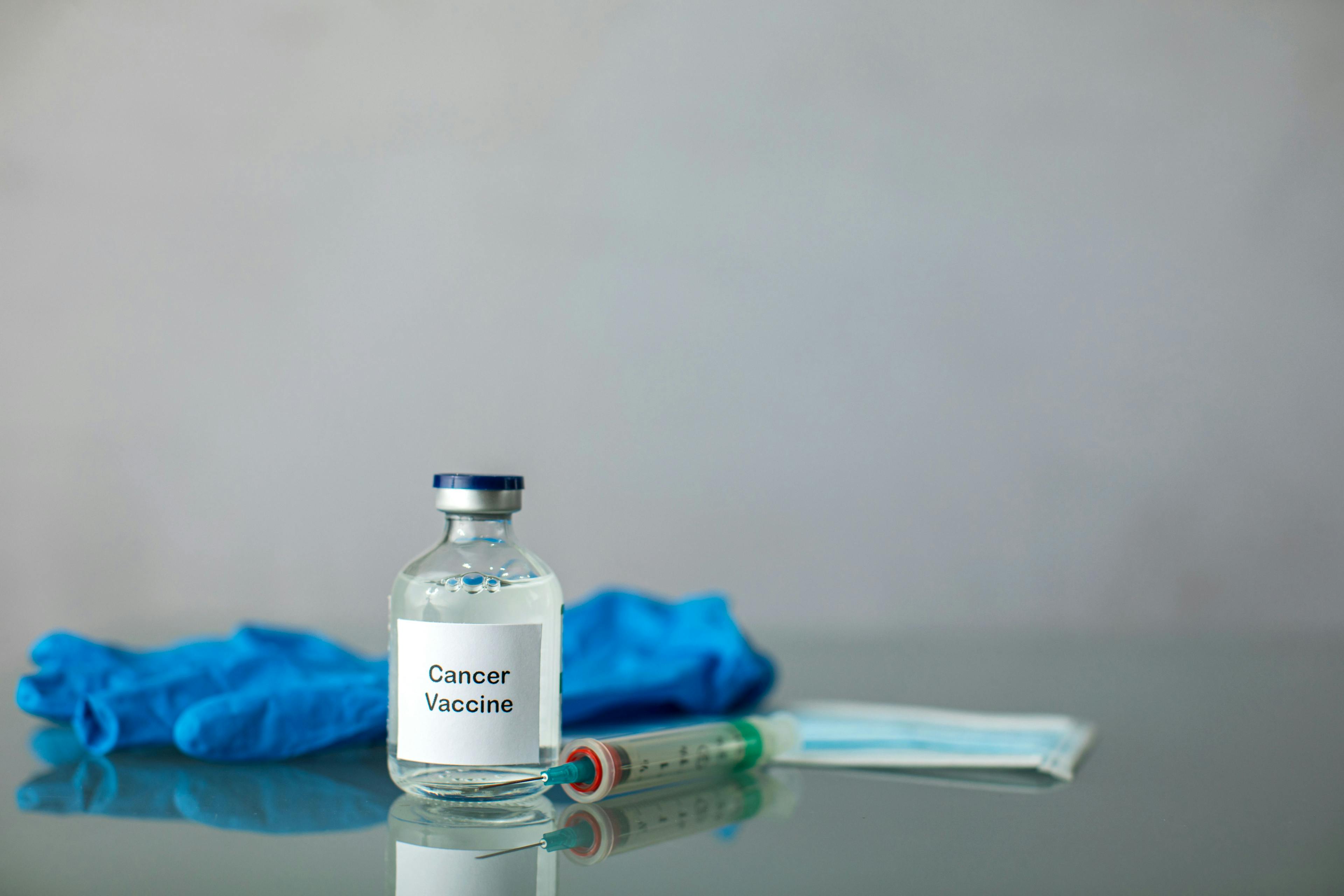 Image of a cancer vaccine vial with a syringe and a blue rubber glove in the background.