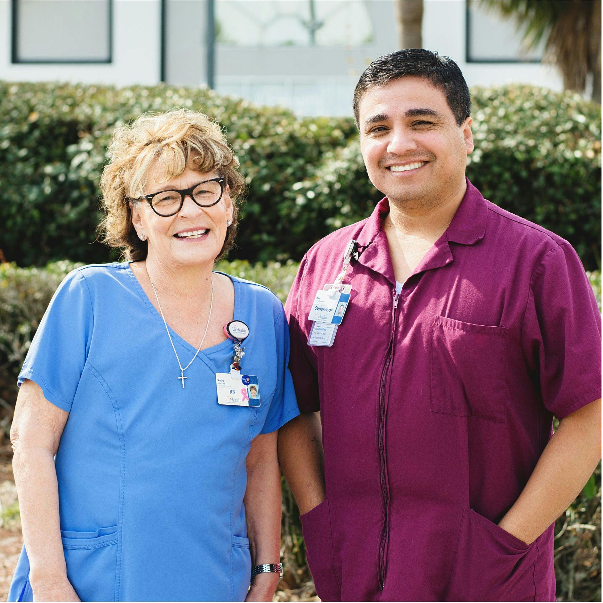 From left: Kelly Bryant, RN, a blonde nurse in blue scrubs with brown glasses and Ides Torres, MLS (ASCP), a Latino man in a maroon scrub top. both are looking at and smiling at the camera  Photos by Marina Kishnir