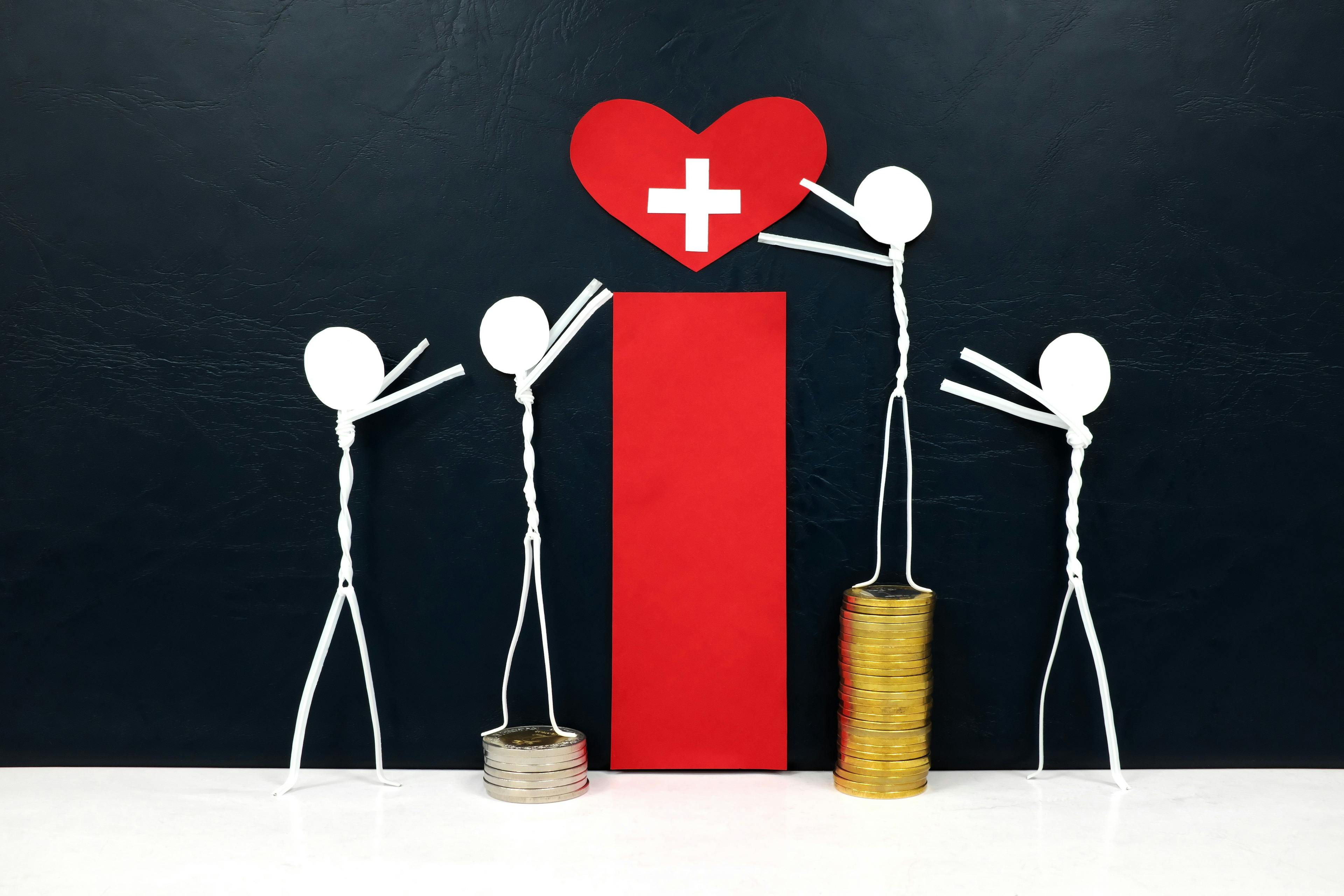 Stick figure reaching for a red heart shape with cross cutout while stepping on stack of coins. Healthcare, medical care and hospital access inequality concept. | Image credit: © sulit.photos © stock.adobe.com