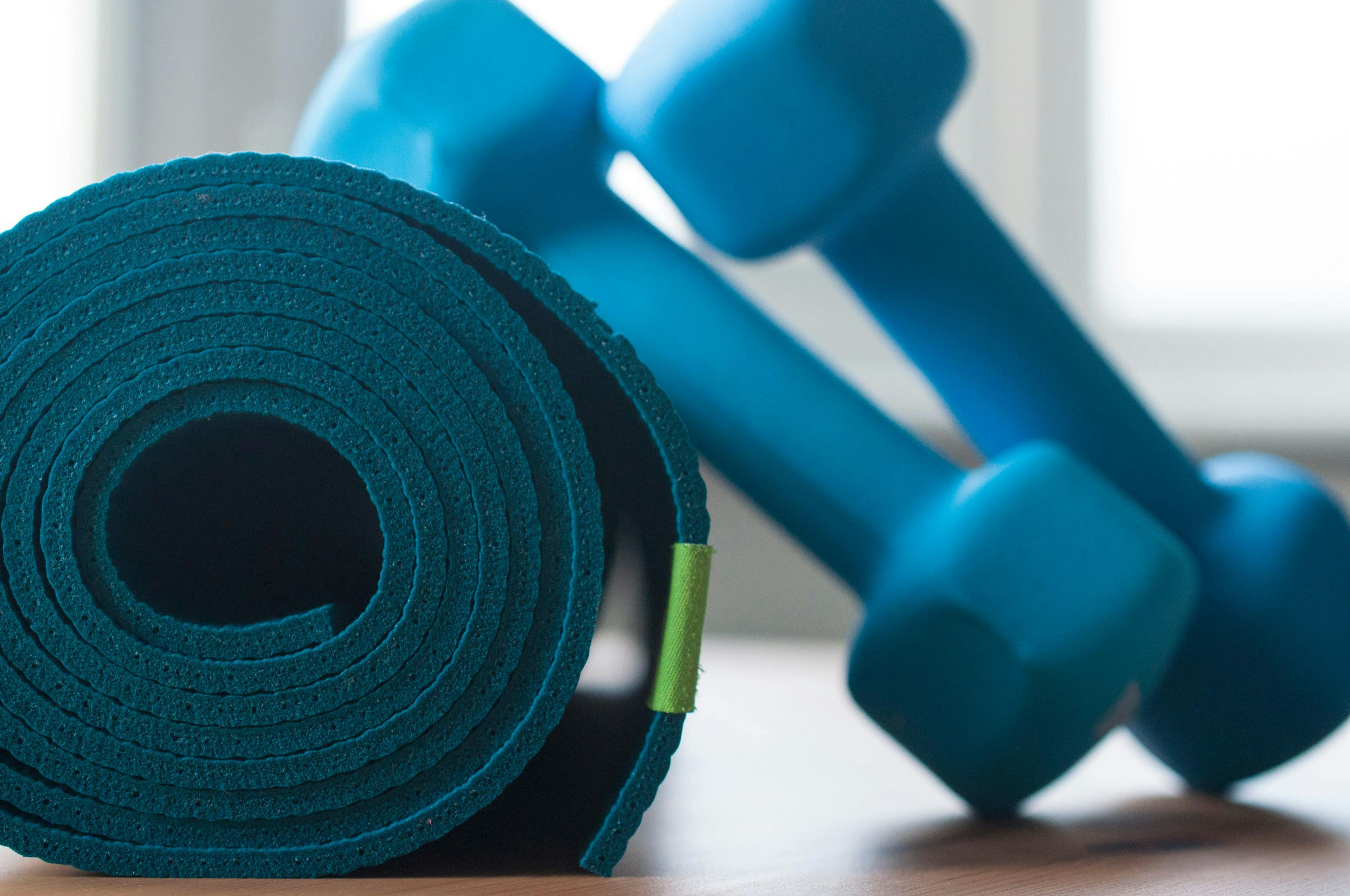 A blue rolled yoga mat. Two blue 2 kg dumbells resting on it. Fitness equipment for home exercise and flexibility training. | Image credit: © Lisa Anastassiu - © stock.adobe.com