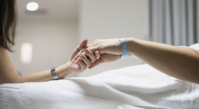 patient in hospital bed holds hand with a caregiver