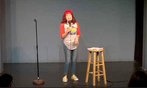 Summer Golden, a MDS survivor, performing stand-up comedy. She is on the stage with a mic in her hand