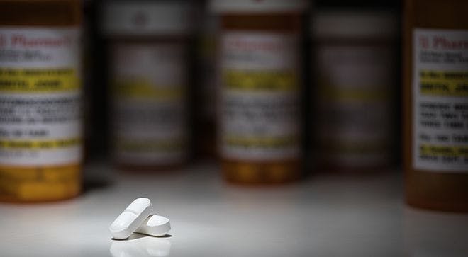 two white pills sitting in front of prescription drug bottles