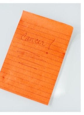 Orange post-it note with the word "Cancer" written on it