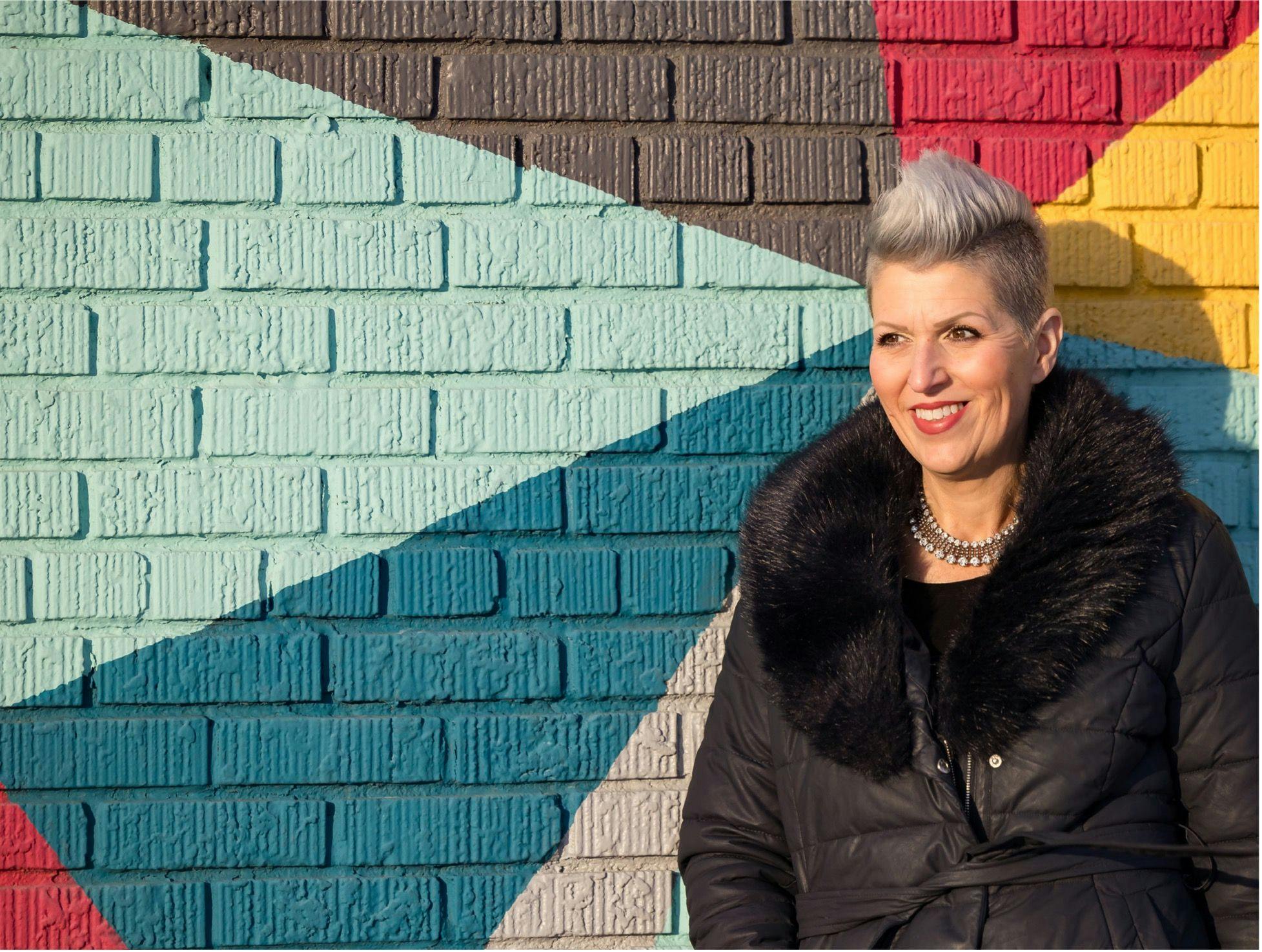 Patient advocate, Heather von St. James, standing in front of a colorful brick wall