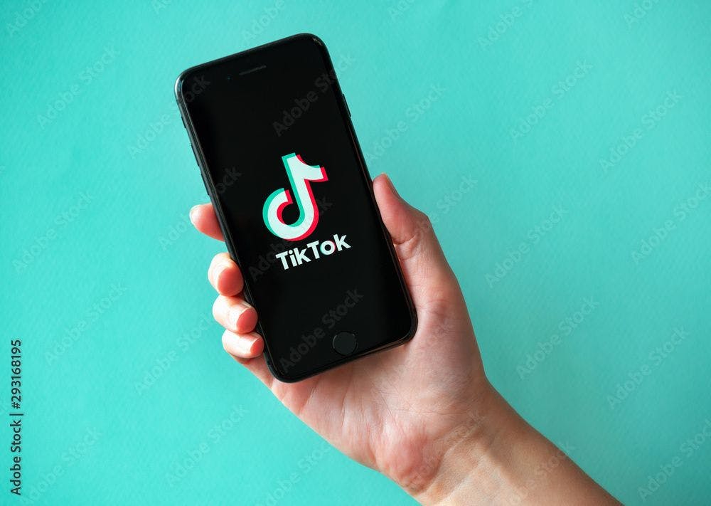 Kyiv, Ukraine - October 1, 2019: Studio shot of hand holding Apple iPhone 8 with TikTok logotype on a screen. Isolated on a vibrant cyan paper background. | Image credit: © - bloomicon © - stock.adobe.com. 