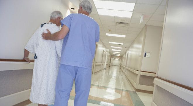 frail older person walking with a man in scrubs down a hospital hallway