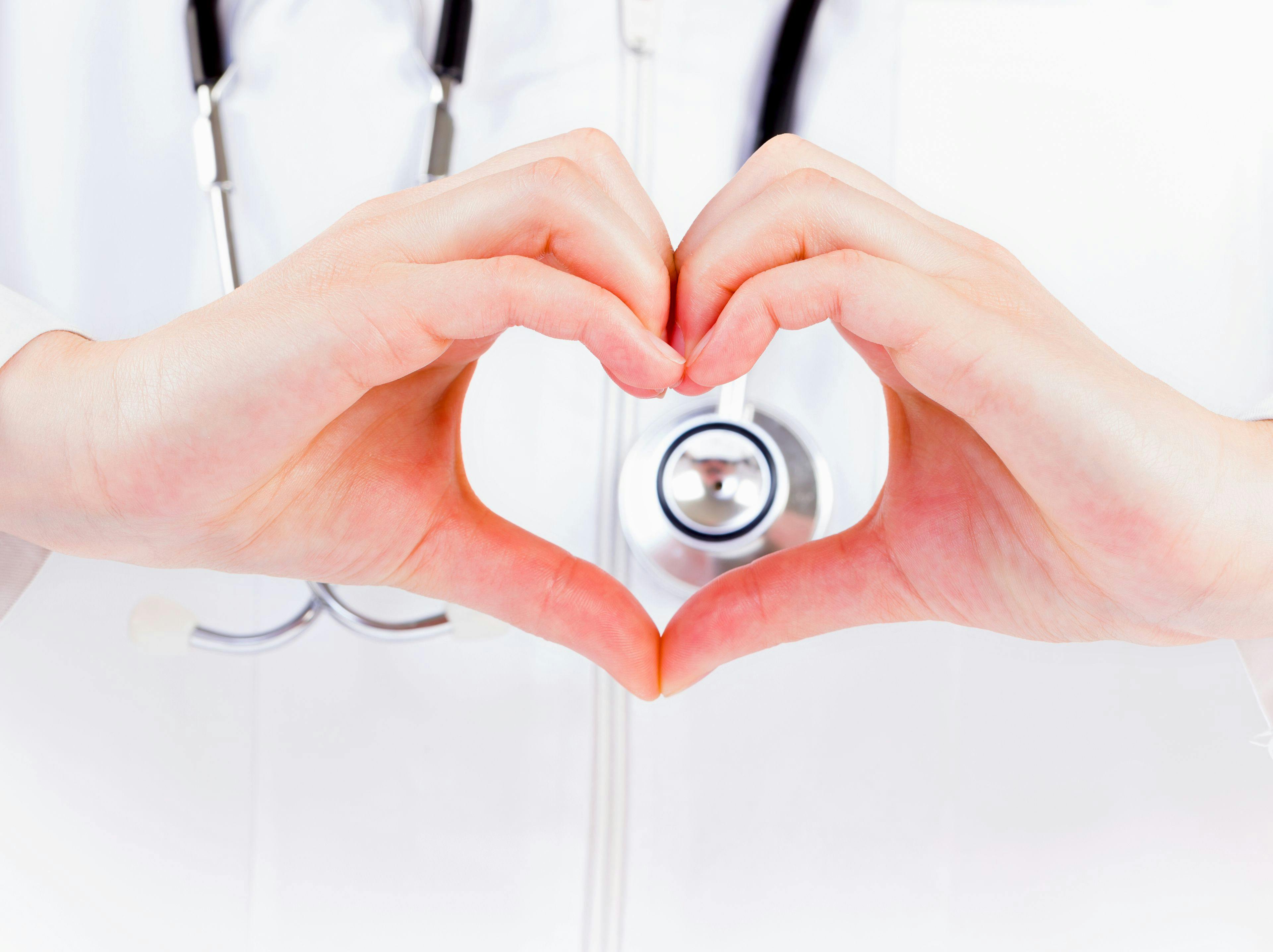 doctor in a white coat with a stethoscope around neck making a heart with her hands