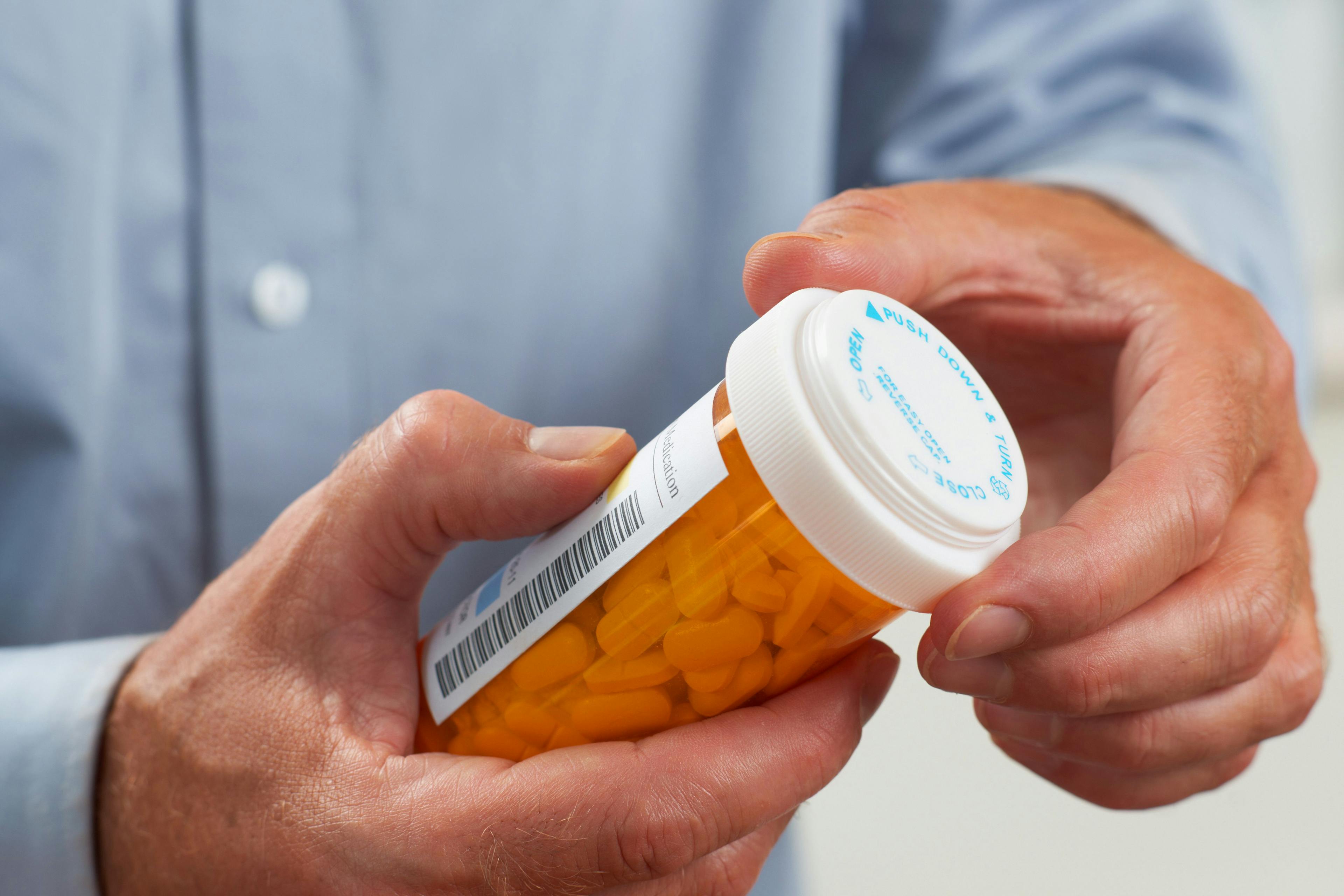 A patient with a blue button-up shirt holding an orange bottle of prescribed pills. ARV-471, a novel oral treatment, could be potentially approved by the FDA after it got a Fast Track designation.
