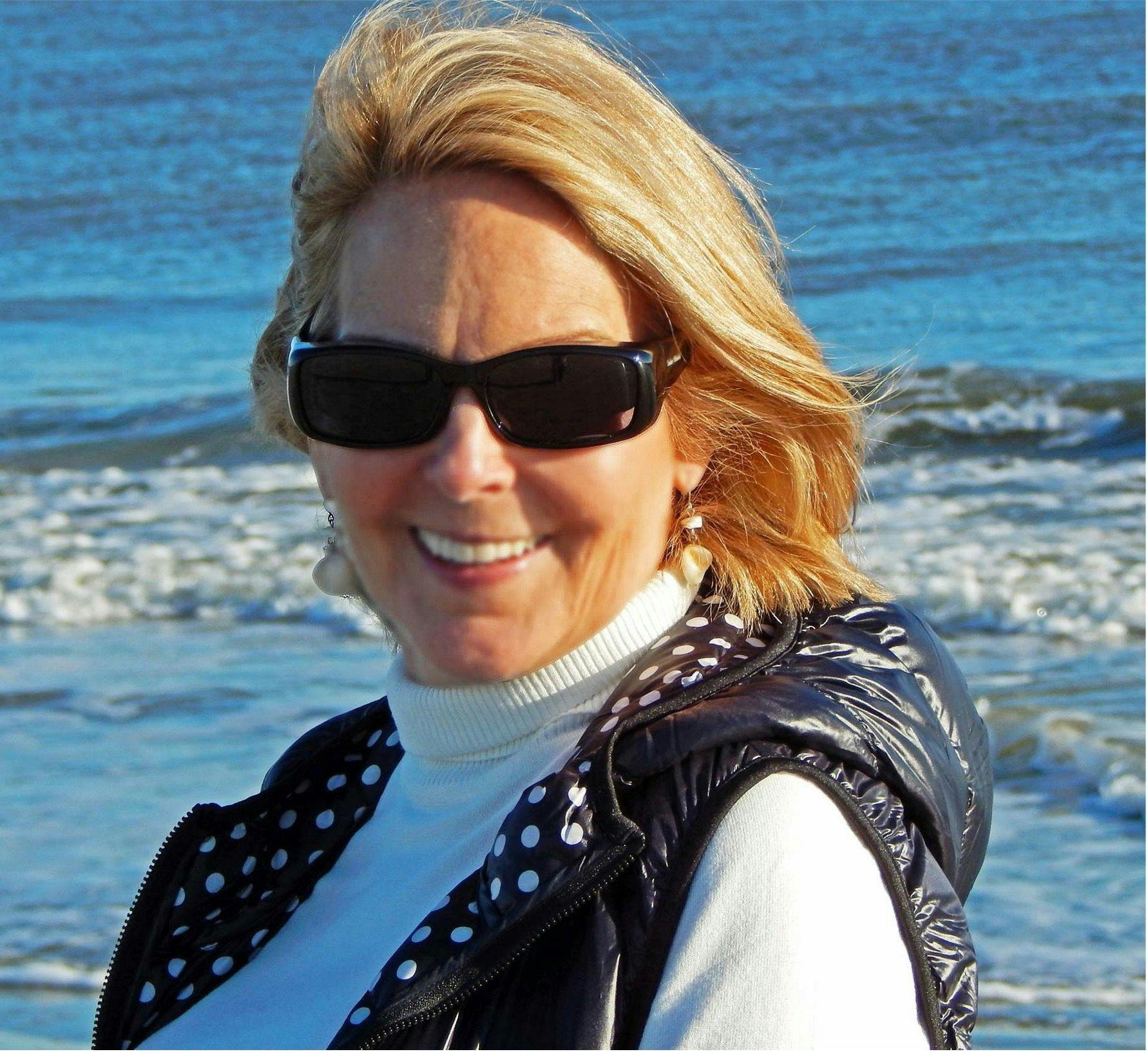 Penny Isop wearing sunglasses and smiling, with the ocean in the background
