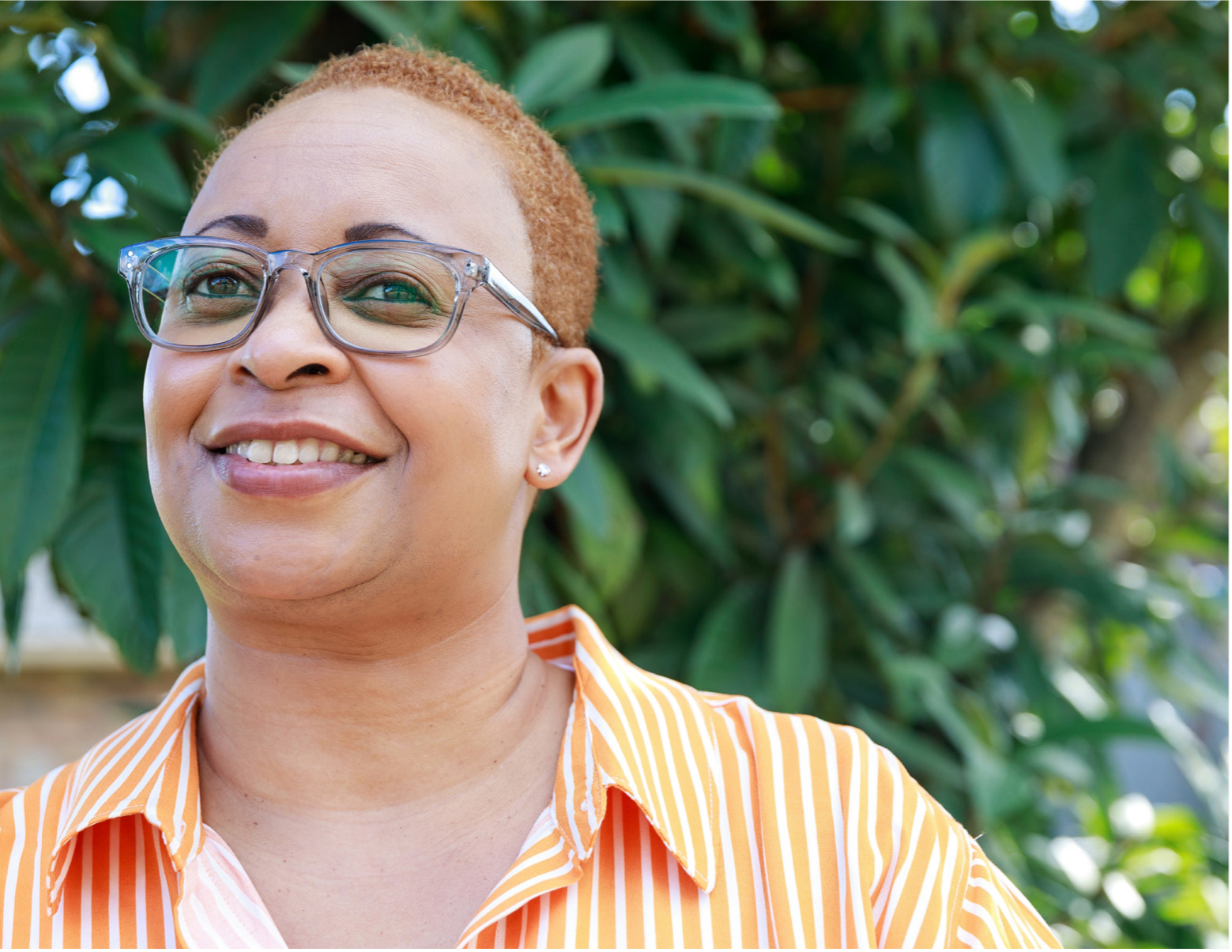 Multiple myeloma survivor, Trena Robertson, a black woman with short hair and glasses, stands in front of a leafy background | Photo credit: Collin Richie