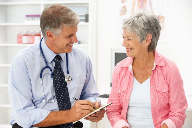 A doctor sitting next to an elderly female patient smiling and holding a clipboard