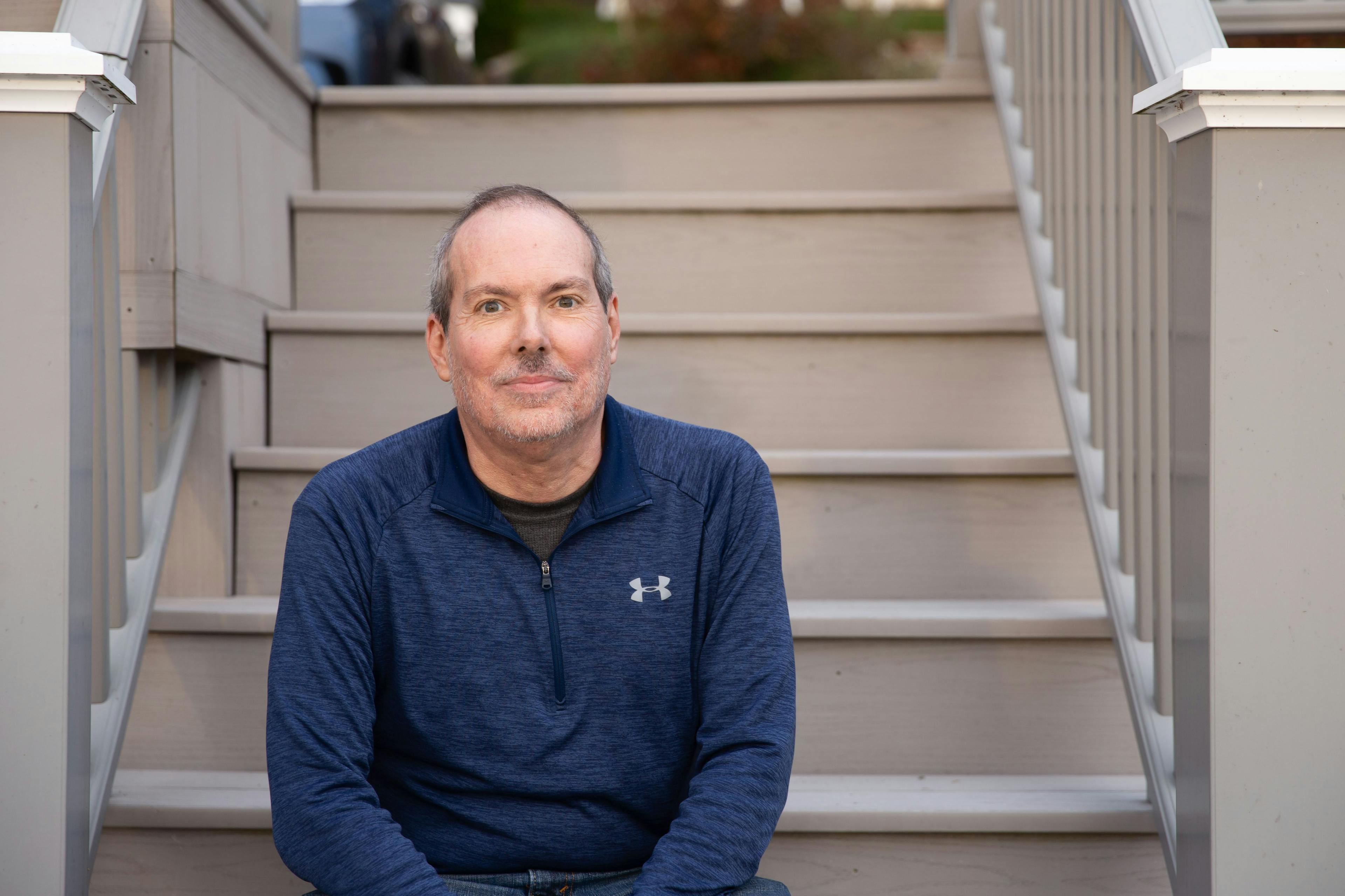 A photo of Jeff Battles wearing a blue sweater, sitting on stairs