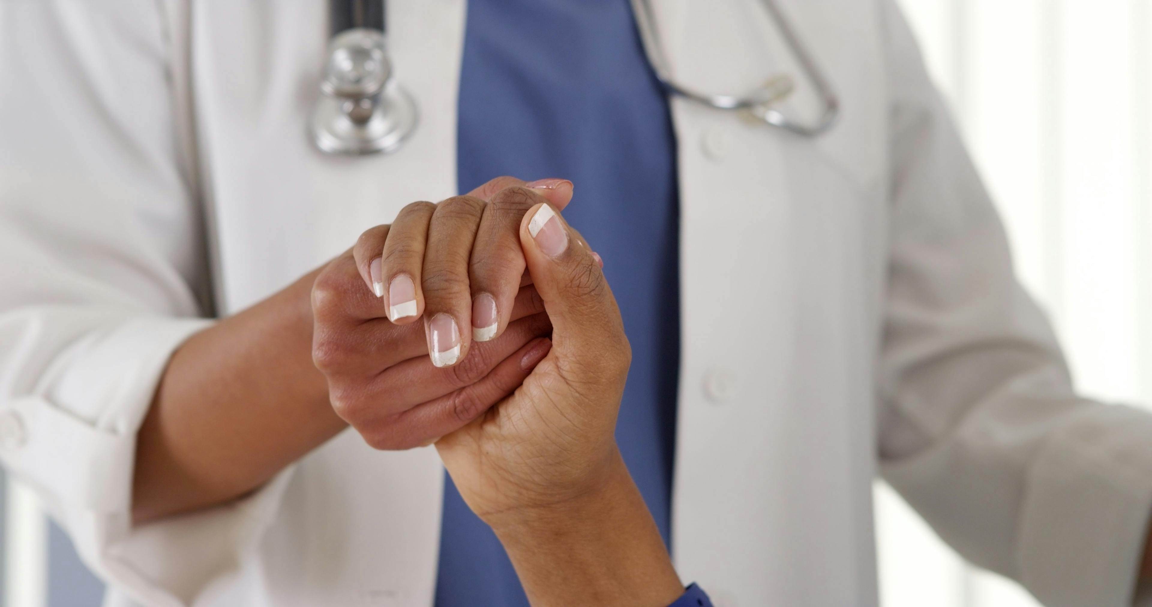 An African American doctor holding the hand of an African American patient