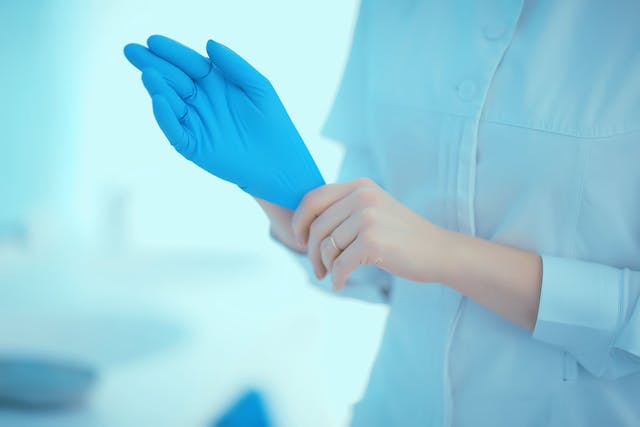 Image of a doctor putting on blue rubber gloves.