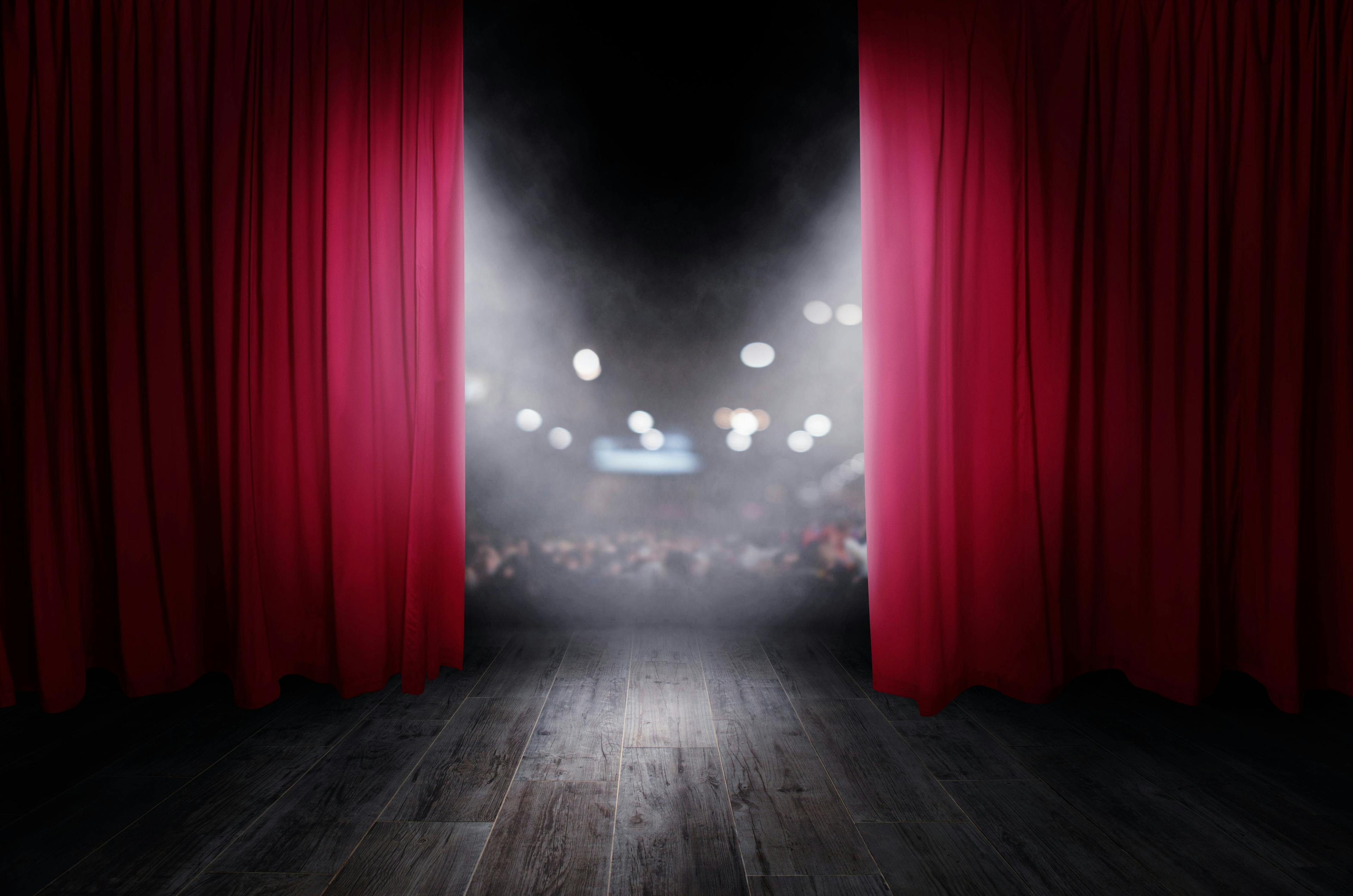 Image of a theatre stage with red curtains and a spotlight in the middle of the stage.
