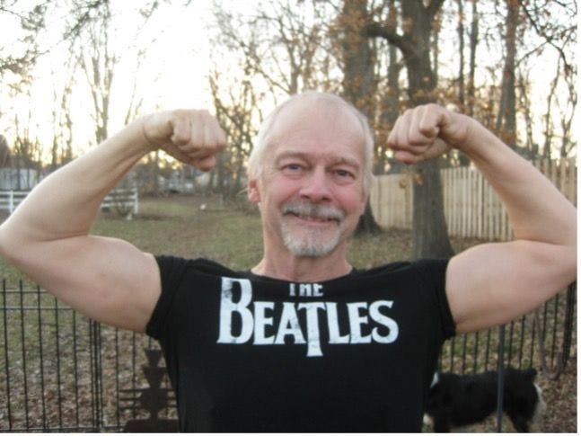 Man wearing a black Beatles shirt, flexing his muscles.