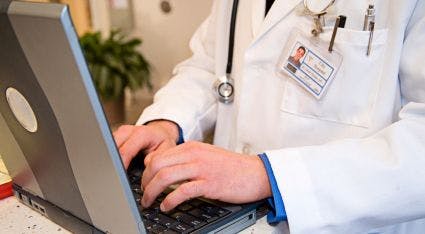 doctor in white coat typing on laptop