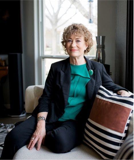 Meg Lowry, an older white woman with short, curly hair, sits on a couch and looks at the camera | Photo credit: Kelly Colson