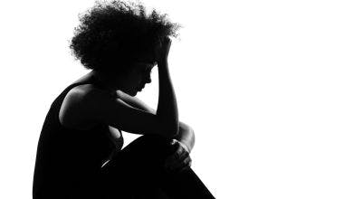 silhouette of depressed woman sitting against a wall with her head in her hands