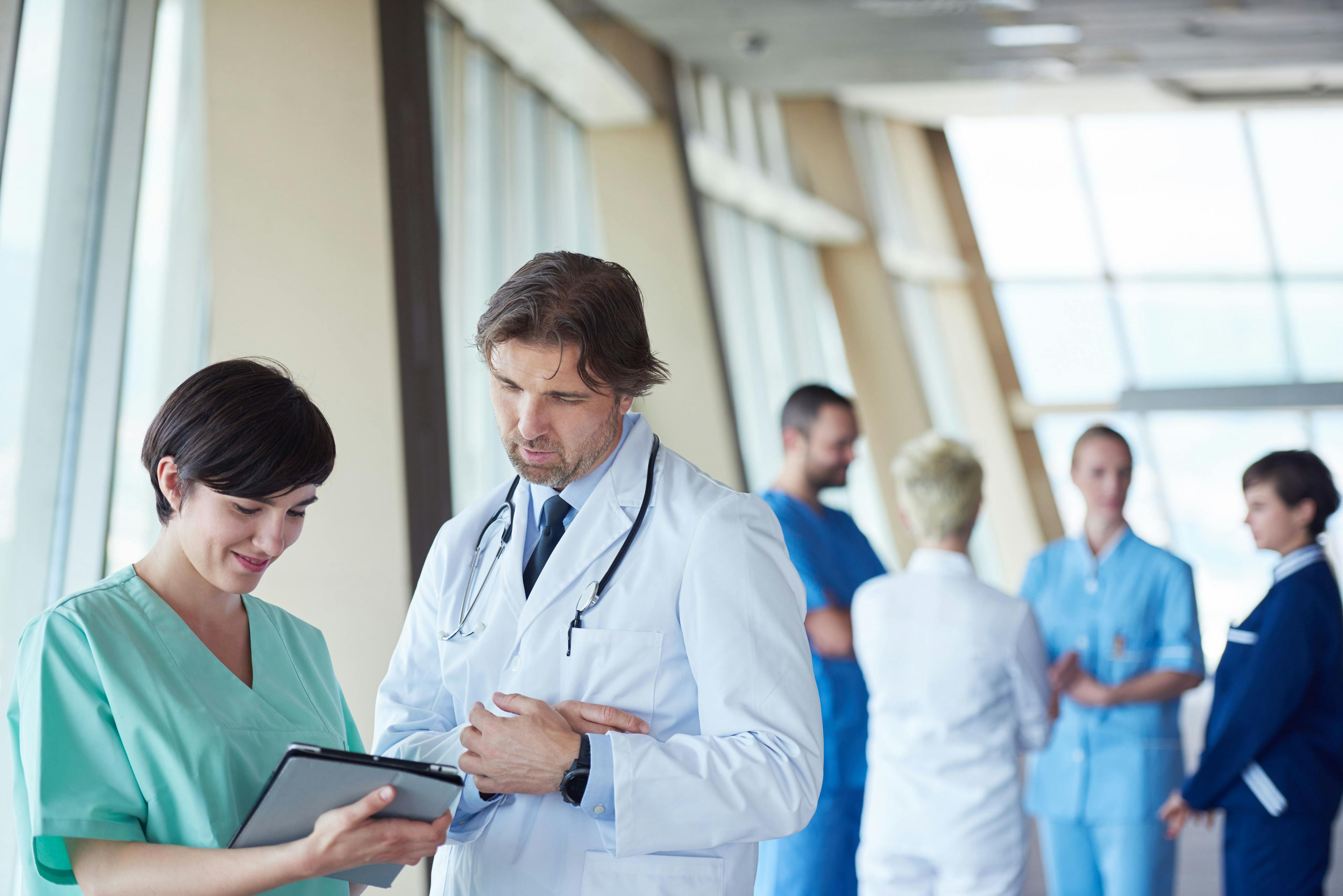 An image of a nurse speaking with a doctor in the foreground with four other medical professionals talking in the background. 